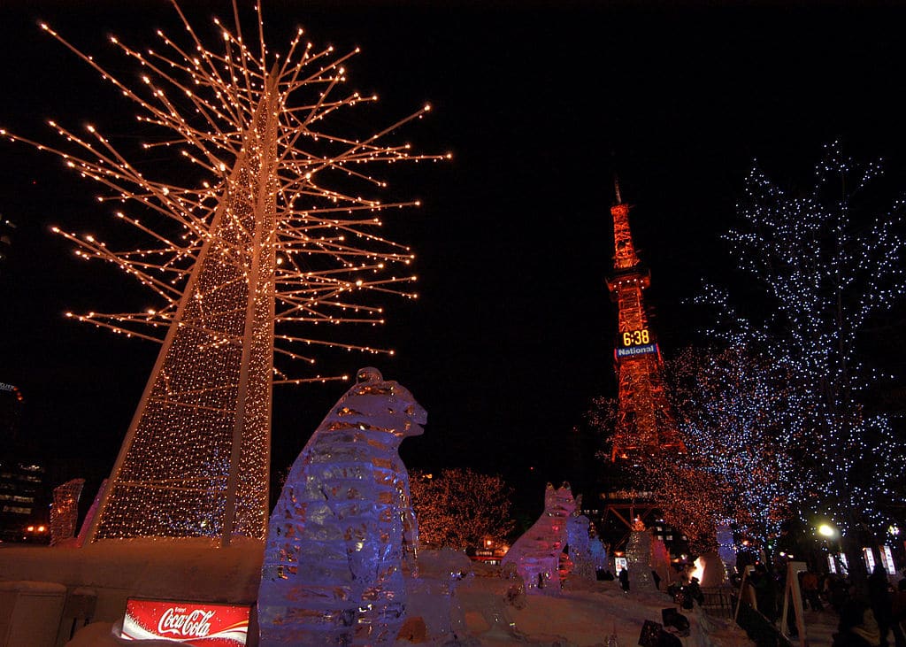 Glowing ice sculptures and winter light displays in Odori Park at night with the Sapporo TV Tower illuminated in the background.