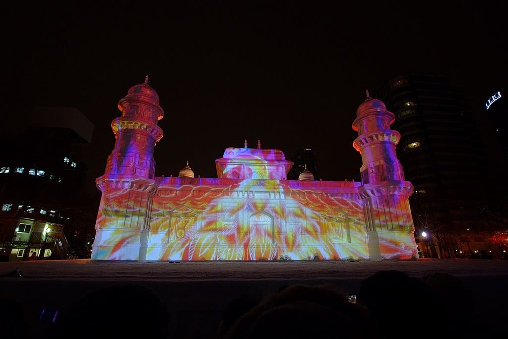 A massive snow sculpture lit with colorful projection mapping that covers the entire structure during a nighttime show in Odori Park.