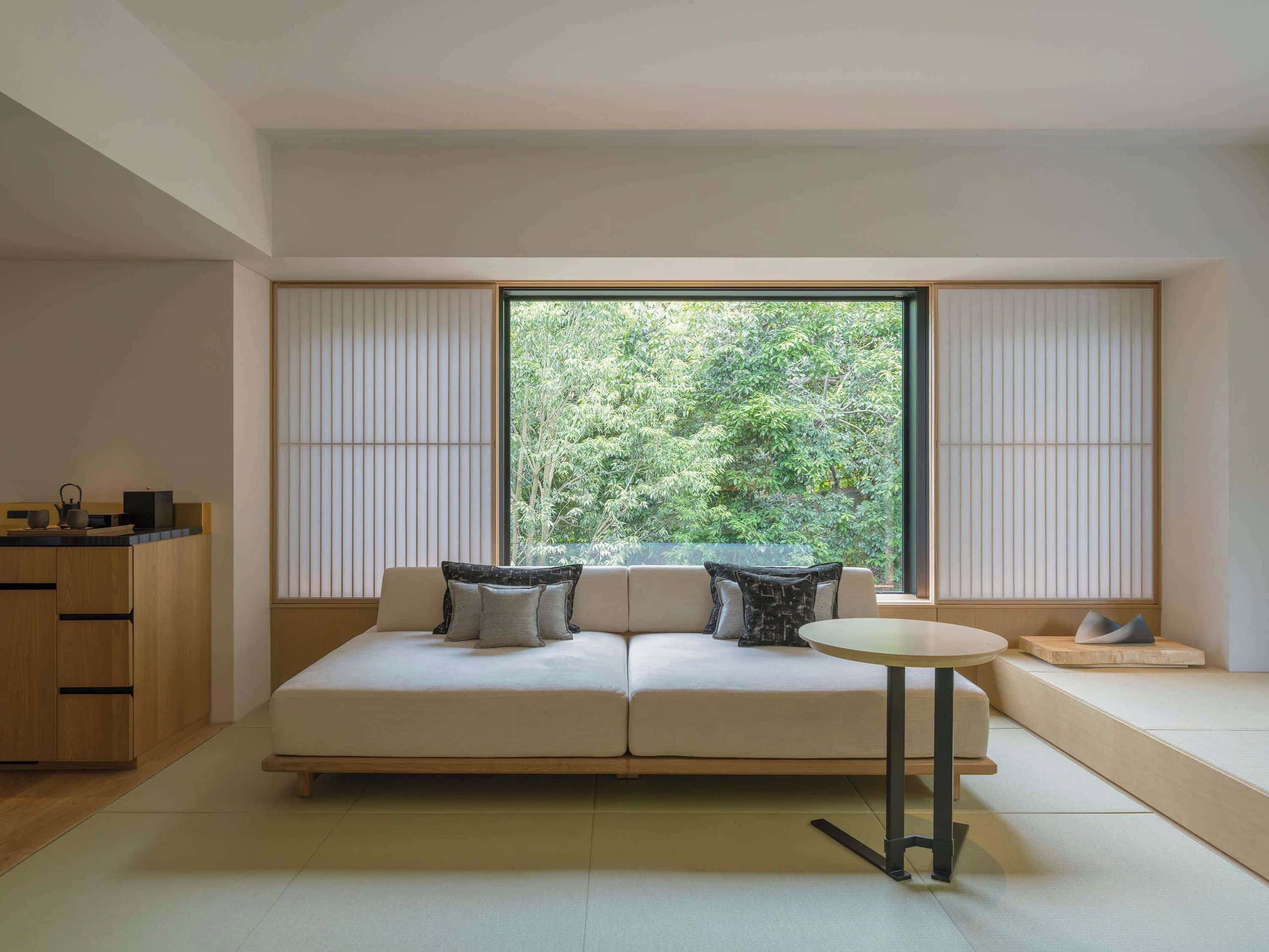 A serene suite at Banyan Tree Higashiyama Kyoto featuring minimalist Japanese design, tatami flooring, and a large window overlooking lush greenery.