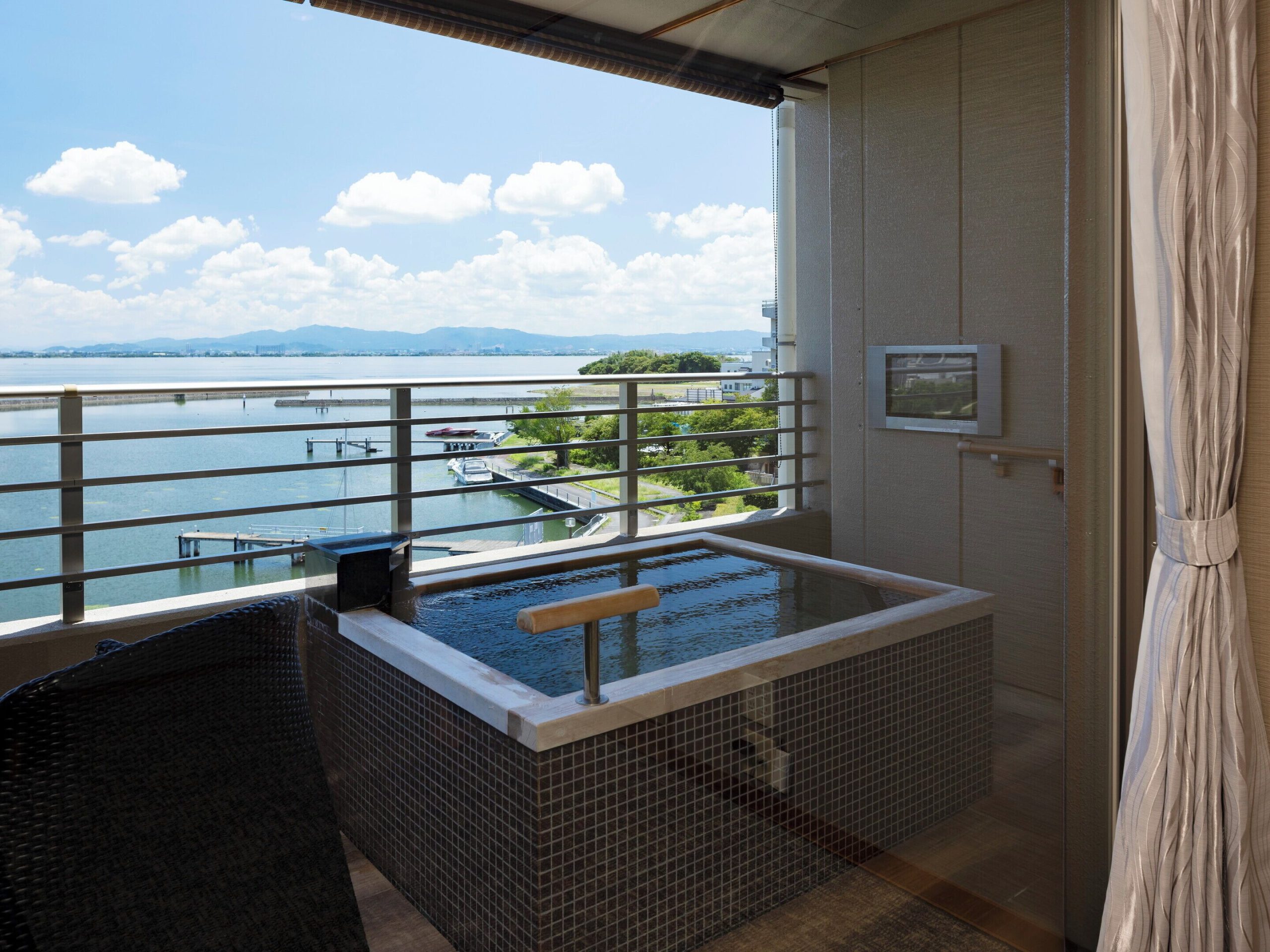 Private balcony onsen at Biwako Ryokusuitei Ryokan overlooking Lake Biwa under a clear blue sky, perfect for relaxing in nature.