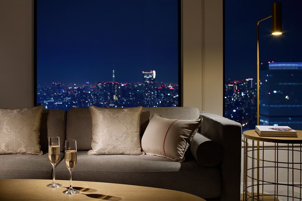 A romantic night view from a suite at Keio Plaza Hotel Tokyo, featuring a cozy sofa, soft lighting, two glasses of champagne, and panoramic city skyline views — capturing why it’s one of the top honeymoon hotels Tokyo offers.