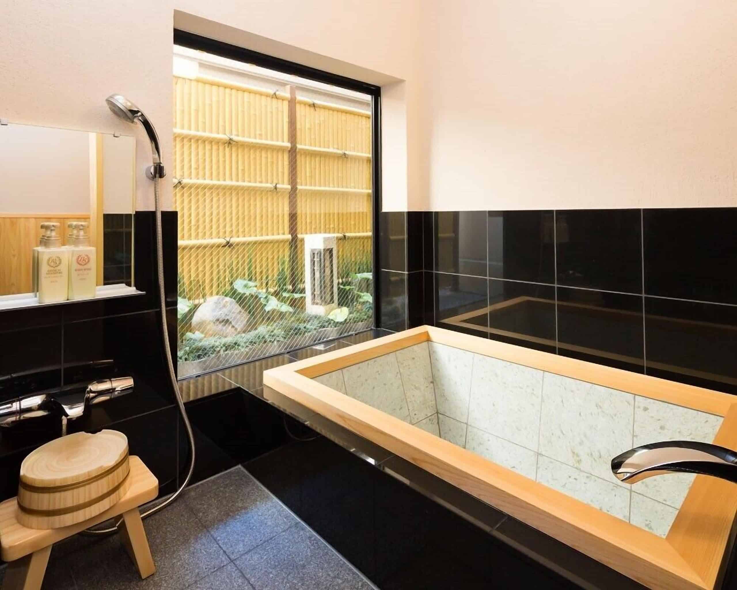 Private hinoki wood bath at Nazuna Kyoto Nijo-jo with a large window overlooking a small Japanese garden, blending elegance and traditional comfort.