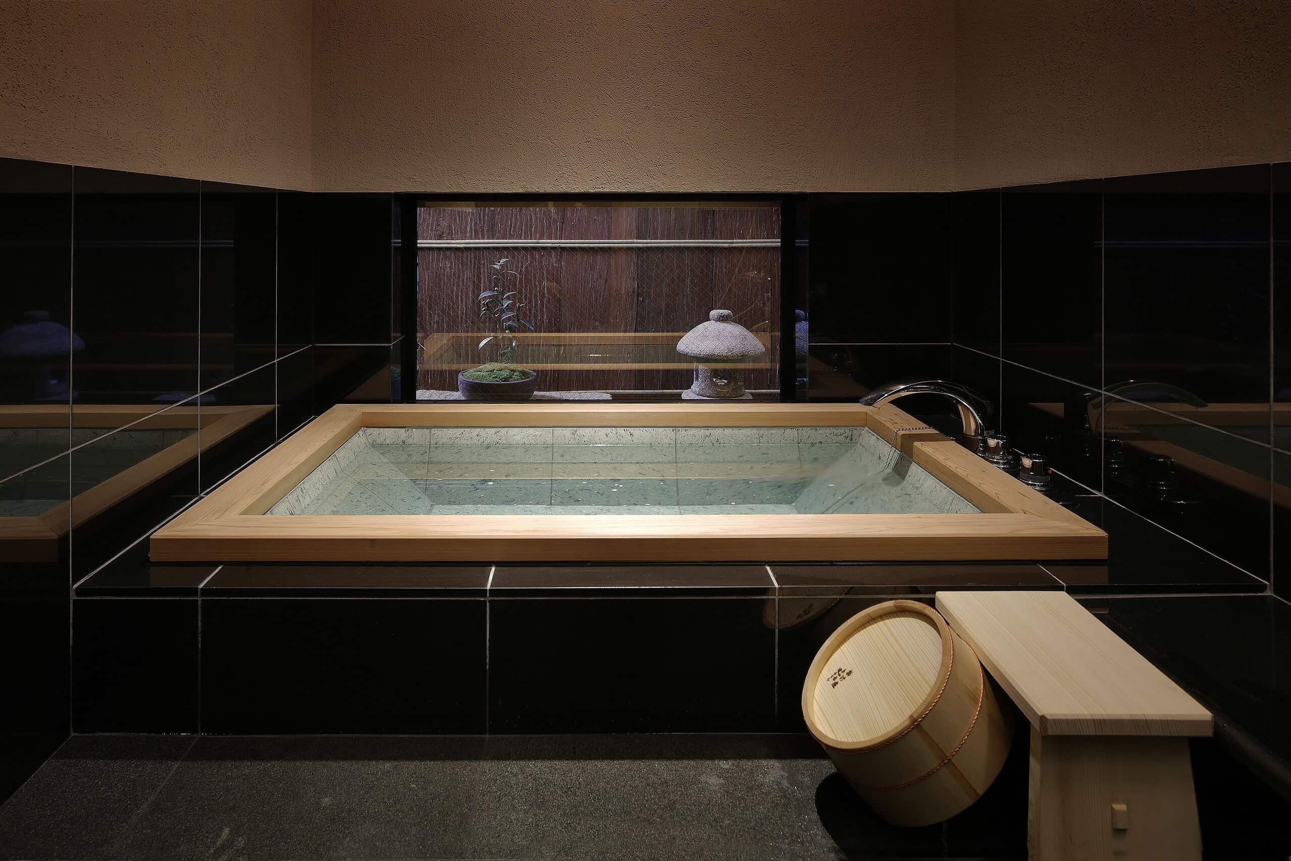 Urushitei Ryokan’s private garden bath offers a serene indoor-outdoor onsen experience with a handcrafted wooden tub and a lush garden view.
