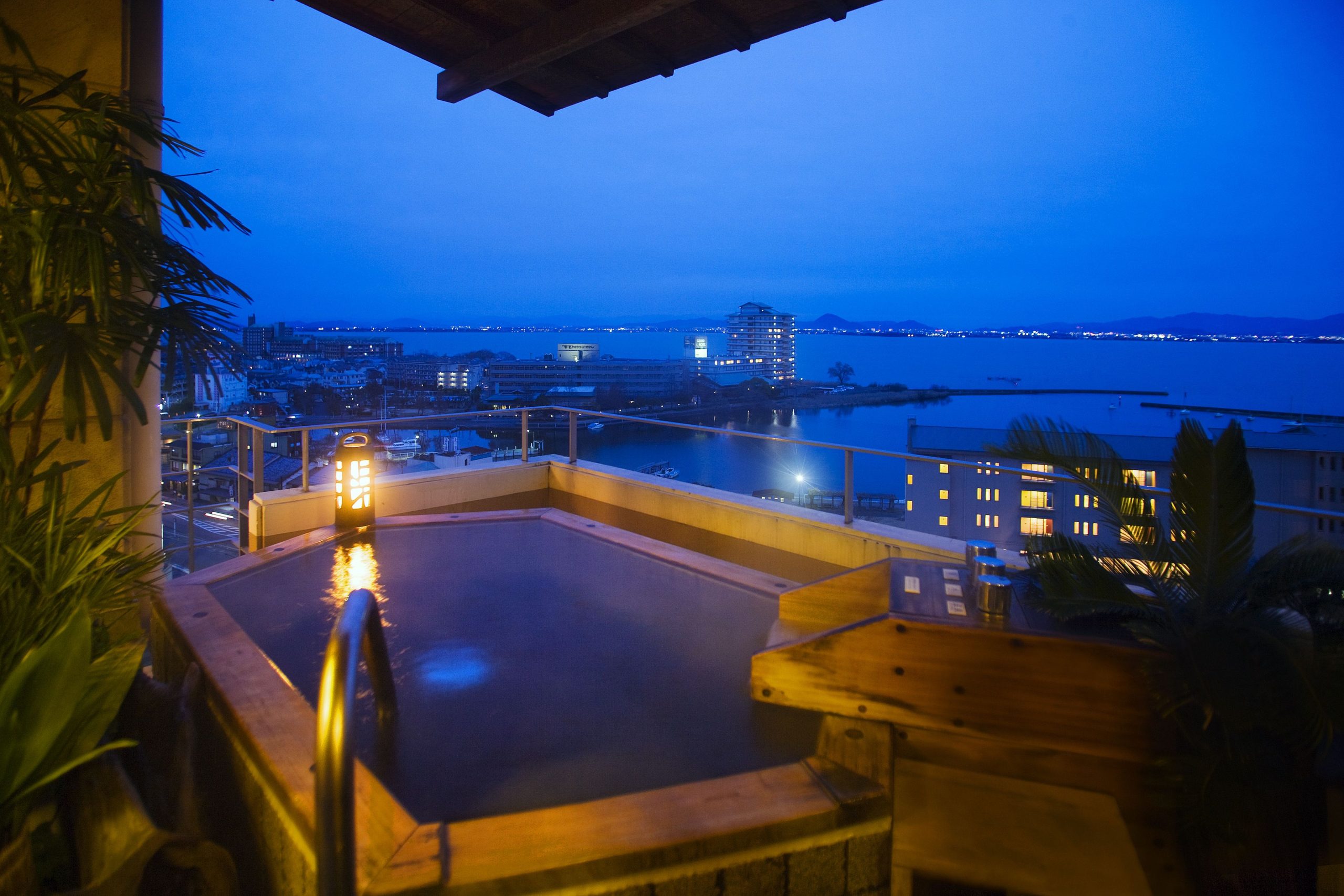 Rooftop onsen at Yumotokan Ryokan with panoramic night views over Lake Biwa and the city lights reflecting on the water.