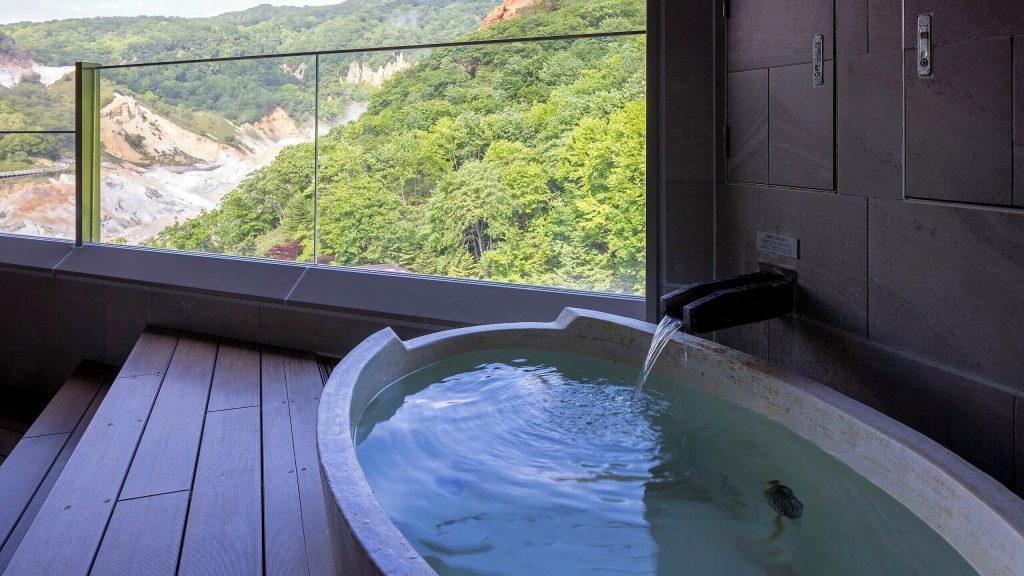 Private onsen bath at Dai-ichi Takimotokan overlooking the dramatic cliffs and lush greenery of Noboribetsu Hell Valley.