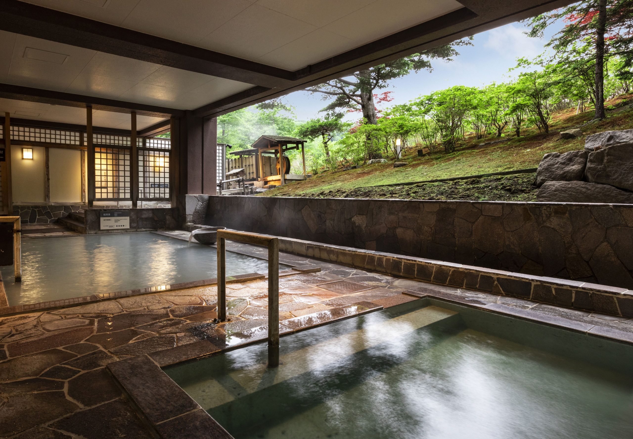 Indoor public hot spring bath at Dai-ichi Takimotokan with an open view of the surrounding garden and greenery in Noboribetsu.