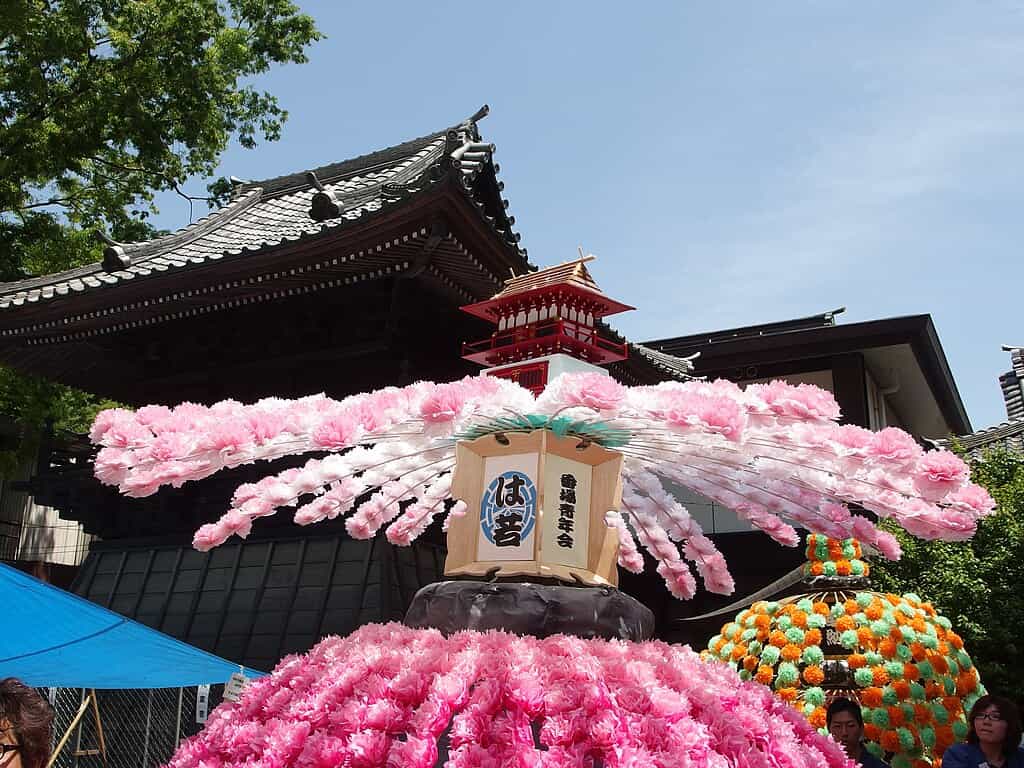 Decorated festival float covered in pink cherry blossom flowers at Kurayami Matsuri in Fuchu, set in front of a traditional shrine building.