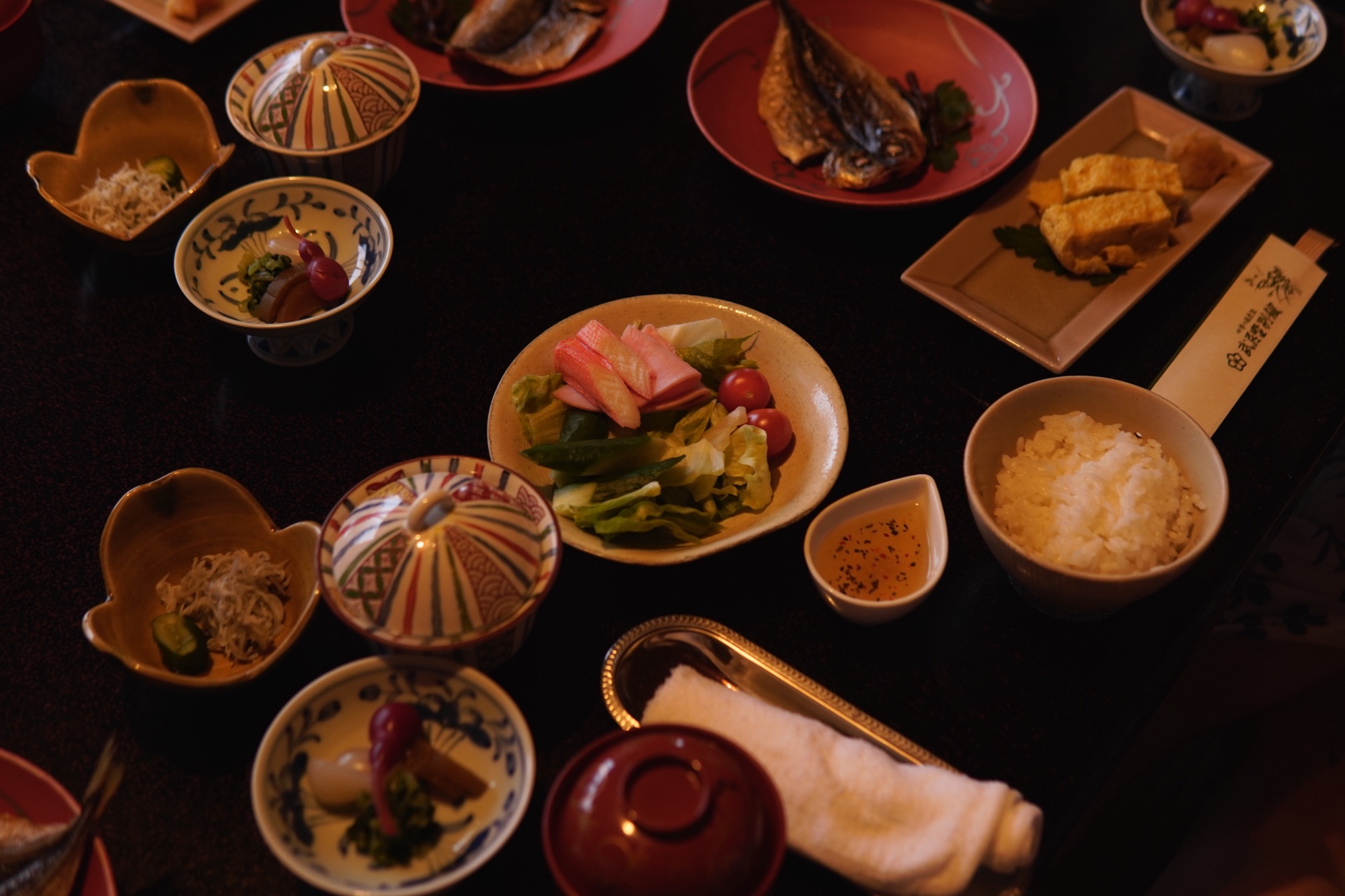 Traditional Japanese kaiseki style meal with rice, grilled fish, vegetables, and small side dishes arranged on a dark table