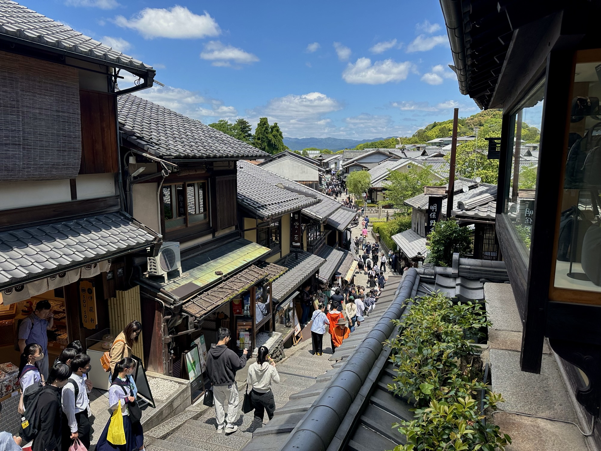 View down the sloping stone street of Sannenzaka lined with traditional wooden buildings, shops, and crowds walking below