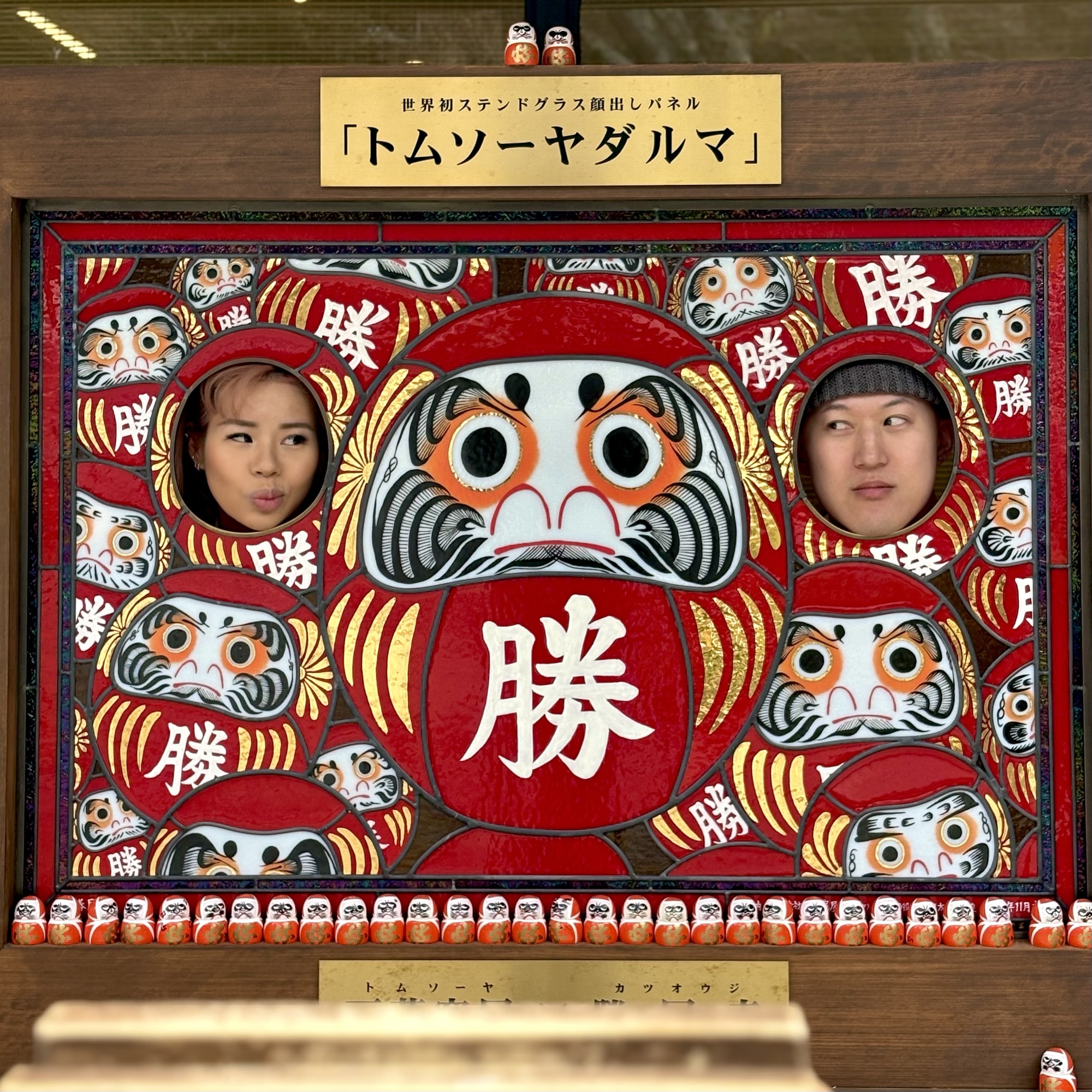 Audrey and Dennis at katsuoji temple near Osaka, making funny faces while posing behind a Daruma doll sign