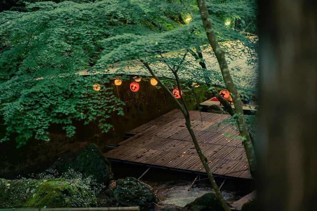 Tranquil kawadoko setting in Kyoto with lush greenery and lanterns.