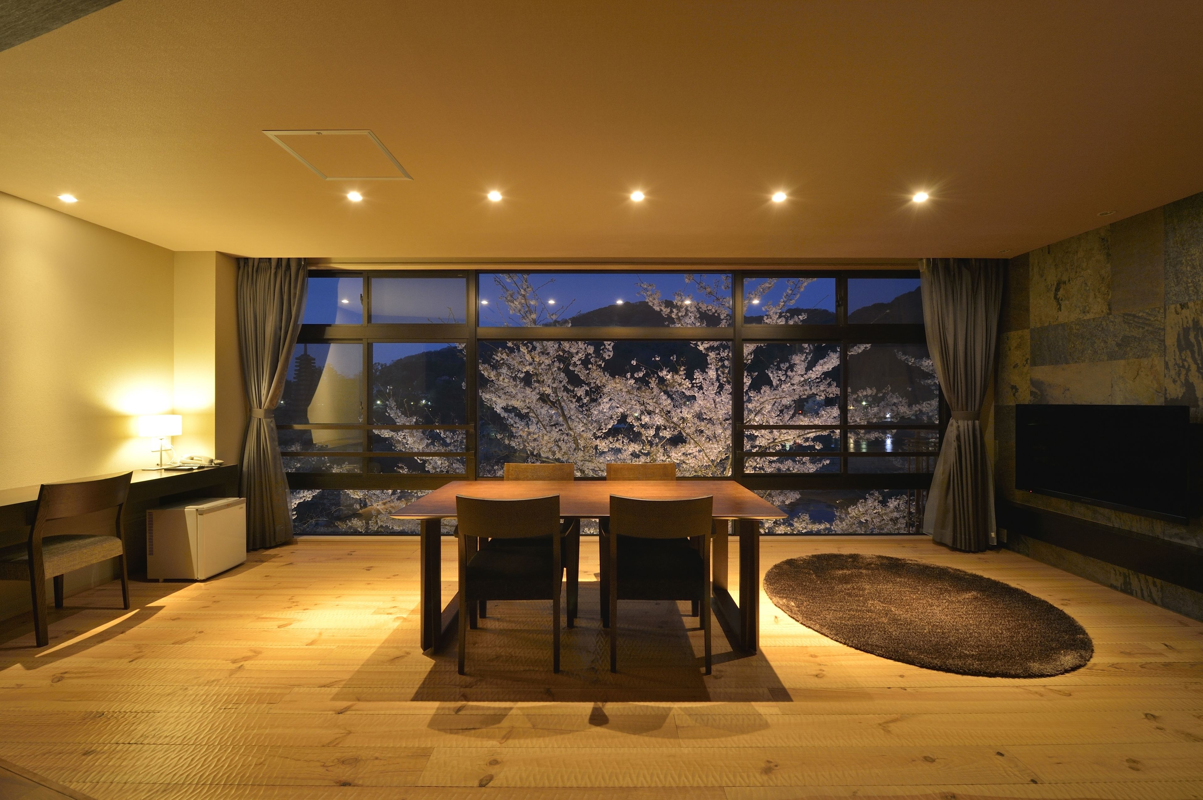 Warmly lit guest room at Hanayashiki Ukifune En with large windows and cherry blossom views at night