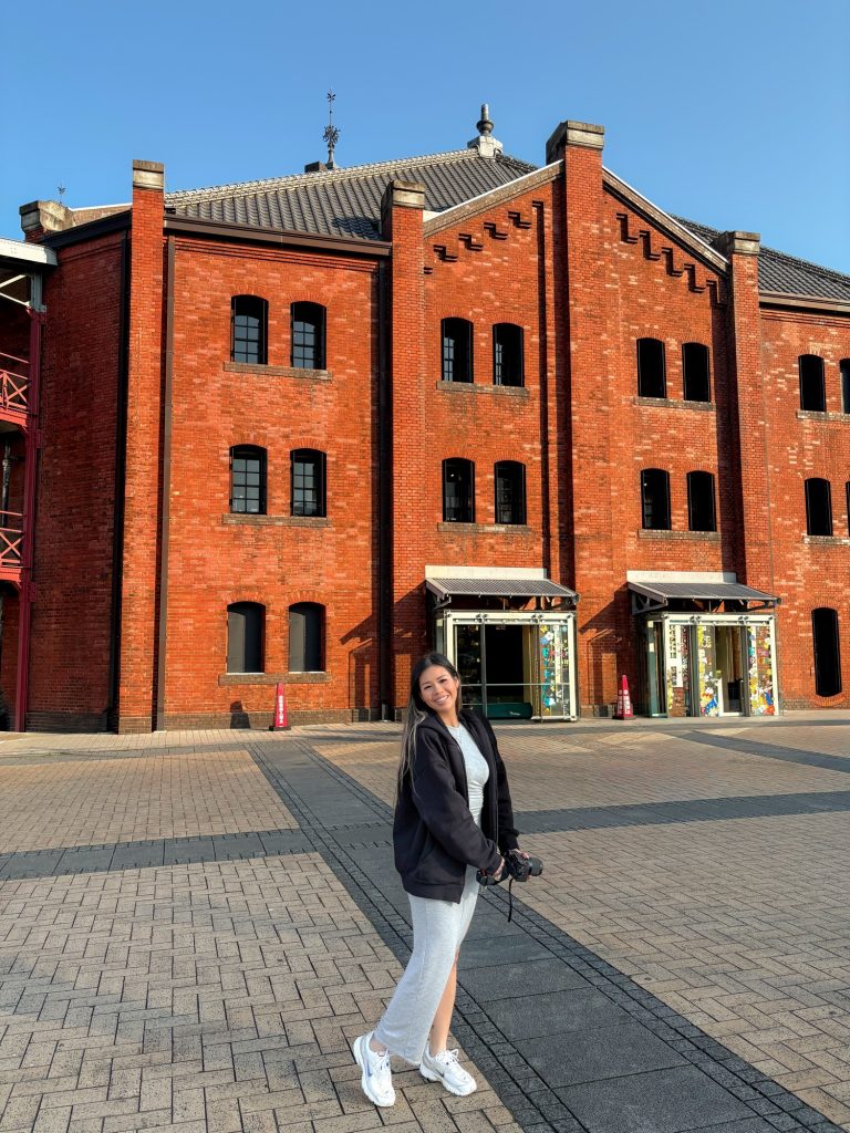 Audrey smiling in front of Yokohama Red Brick Warehouse while holding her camera.