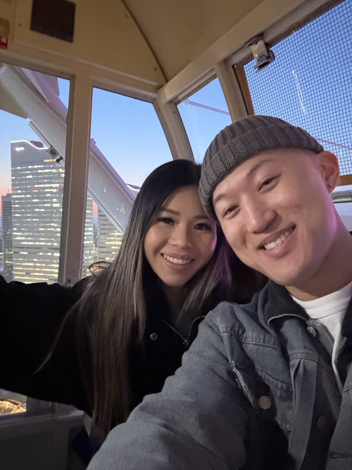 Audrey and Dennis smiling inside the Cosmo World Ferris wheel with Yokohama city buildings outside the window.